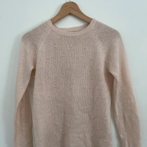 Beige stickad tröja med pärlor från House - Säljer en söt beige stickad tröja från House, dekorerad med små pärlor över hela framsidan. Tröjan har långa ärmar och en rund halsringning. Perfekt för att ge en elegant touch till din outfit. 
