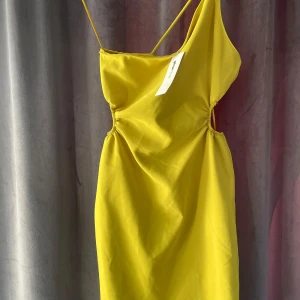 Gul axelbandslös klänning från Gina Tricot  - Snygg gul grön klänning från Gina Tricot med en axelbandslös design och smala axelband. Klänningen har en figurnära passform och rynkade detaljer på sidorna som ger en fin siluett. Perfekt för sommarens alla tillfällen! 🌞 