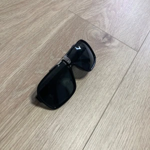 Svarta carrera solglasögon med gulddetaljer - Snygga svarta carrera solglasögon med breda bågar och stilrena gulddetaljer på sidorna. Perfekta för en cool look i solen. Passar både till vardag och fest.