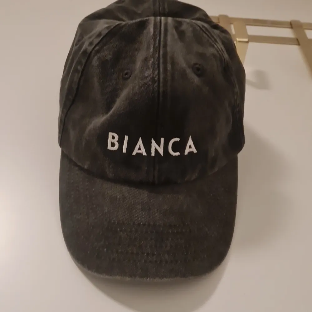 Snygg svart keps med broderad text 'BIANCA' framtill. Kepsen har en justerbar rem baktill för perfekt passform. Perfekt för en avslappnad stil.. Asusteet.