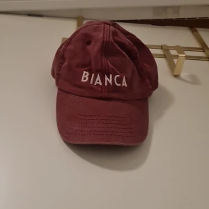 Vinröd keps med broderad text - Snygg vinröd keps med broderad text 'BIANCA' framtill och 'Coca-Cola' baktill. Perfekt för en avslappnad stil med justerbar passform.