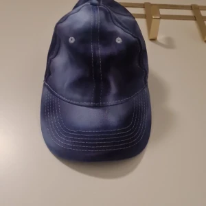 Blå keps med justerbart spänne - Snygg blå keps med vit söm och justerbart spänne baktill. Perfekt för en avslappnad stil.