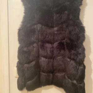 Svart pälsväst - Snygg svart pälsväst som ger en lyxig känsla. Perfekt för att hålla sig varm och stilren under kyligare dagar. Västen har en mjuk och fluffig textur som gör den både bekväm och trendig.