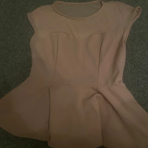 Beige blus med peplum - Säljer en stilren beige blus med peplumdetalj. Blusen har korta ärmar och en rund halsringning. Perfekt för en elegant look. aldrig använt 
