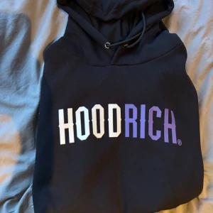 Svart hoodie från Hoodrich - Säljer en svart hoodie från Hoodrich med stor textlogga i vitt och lila på framsidan. Säljer pågrund av att den var för stor för mig. Använd typ 2 gånger så den är ny skick. SKICKAR MED POSTNORD