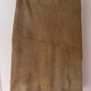 Beige mockakjol från Vespucci - Snygg beige långkjol i mocka från Vespucci. Kjolen har en stilren design med en subtil asymmetrisk detalj framtill och en dragkedja baktill för enkel påklädning. Perfekt för en elegant och sofistikerad look.