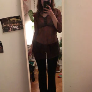 Transparent tunika med mönster - Säljer en transparent tunika med ett subtilt mönster i mörka nyanser. Tunikan har trekvartsärmar och en knytning i midjan för en justerbar passform. Perfekt för lager-på-lager-stil.