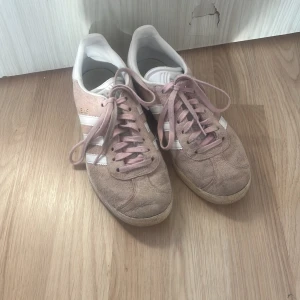Adidas Gazelle i rosa mocka - Säljer ett par klassiska Adidas Gazelle sneakers i rosa mocka med vita detaljer och snörning. Perfekta för en avslappnad stil. Är typ använda 5 gånger