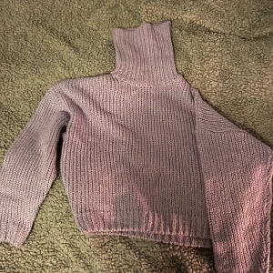 Lila stickad polotröja - Säljer en mysig lila stickad polotröja med hög krage. Tröjan har långa ärmar och ribbstickade detaljer vid ärmslut och nederkant. Perfekt för kyliga dagar!
