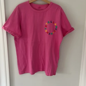 Rosa t-shirt från Stella McCartney  - Säljer en cool rosa t-shirt från Stella McCartney med färgglatt tryck på bröstet. T-shirten har korta ärmar och en rund halsringning. Frakt ingår inte i priset!