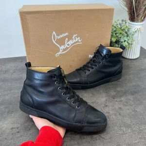 Svarta sneakers från Christian Louboutin - Snygga svarta sneakers i skinn från Christian Louboutin med klassisk röd sula. Skorna har snörning och en rund tå, vilket ger en stilren look. Perfekta för dig som vill ha en touch av lyx i vardagen.