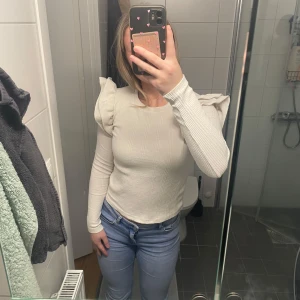 Vit ribbad tröja från Zara - Säljer en stilren vit ribbad tröja från Zara med volangdetaljer på axlarna. Tröjan har långa ärmar och en rund halsringning. Perfekt för en chic och trendig look. Går att pruta 