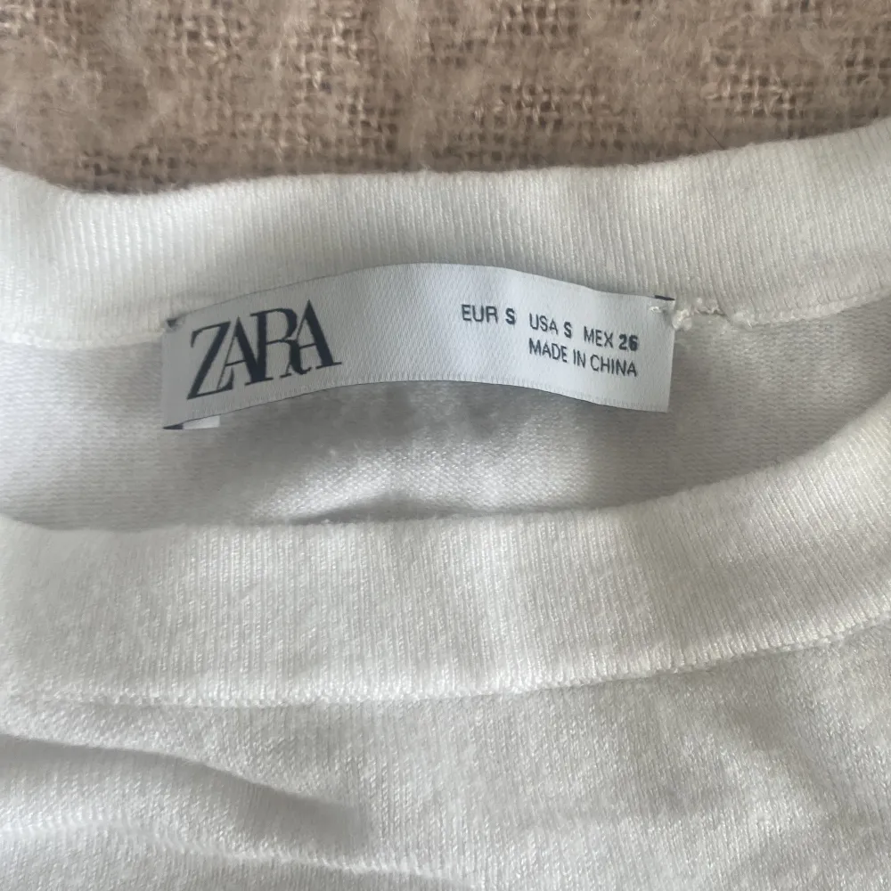 Säljer en stilren vit topp från Zara. Den är kortärmad och har en ribbad kant vid ärmslut och nederkant. Perfekt för en enkel och fräsch look. Passar bra till jeans eller kjol.. Yläosat.