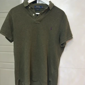 Olivgrön pikétröja från Ralph Lauren - Säljer en stilren olivgrön pikétröja från Ralph Lauren. Tröjan har en klassisk krage med knappar och en liten broderad logga på bröstet. Perfekt för en avslappnad men ändå snygg look.