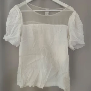Vit topp från Vila - Säljer en elegant vit blus från Vila med transparenta detaljer upptill och puffiga korta ärmar. Passar strl s-m💫