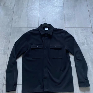 Svart overshirt  - Svart overshirt från Selected Homme, Storlek L. Inköpt drygt 1 år sedan men mest använd förra hösten. Den är i fint skick förutom ”rivmärken” (se 2a bilden). Inget man der jätte tydligt.
