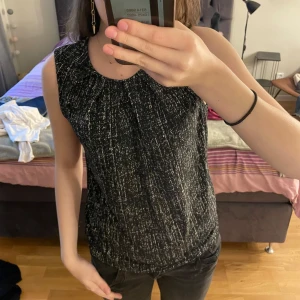 Svart och vit ärmlös topp - Snygg svart och vit ärmlös topp med ett diskret mönster. Toppen har en rund halsringning och en bekväm passform.