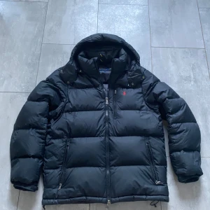 Svart jacka Ralph Lauren - Mattsvart dunjacka från Ralph Lauren i storlek L. Använd vintern 2024 och har bara hängt denna vintern. Den är i fint skick förutom att dragkedjan på luvan är trasig, den är ihopsydd så den sitter fast (Se bild 3). Det är inget man ser men det gör att luvan inte går att ta av.