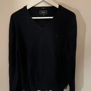 Mörkblå v-ringad sweatshirt tröja från boomerang - Säljer en stilren svart v-ringad tröja från  boomerang. Tröjan har långa ärmar och en diskret logga på bröstet. Perfekt för en klassisk och tidlös look.