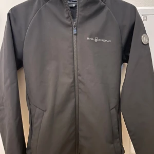 Svart jacka från Sail Racing - Säljer en svart jacka från Sail Racing. Jackan har en dragkedja framtill och en diskret logga på framsidan 