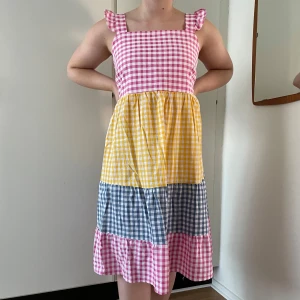 Flerfärgad rutig klänning - Charmig klänning med rutigt mönster i rosa, gul och blå. Den har breda axelband och en smockad rygg för bekväm passform - egensydd, aldrig använd.  @sytanten_ (Instagram)