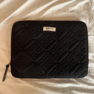 Svart quiltad datorväska från DAY ET - Snygg och praktisk svart quiltad datorväska från DAY ET. Väskan har en dragkedja upptill och är perfekt för att skydda din laptop. Den quiltade designen ger ett stilrent intryck och den är lätt att bära med sig. Nypris 400kr. 