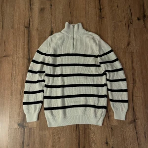 Vit och svart randig tröja med dragkedja från Zara - Snygg vit tröja med blå ränder och en halv dragkedja vid halsen. Perfekt för en stilren look. Tröjan har långa ärmar och är ribbad för extra komfort.