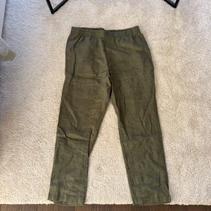 Gröna linnebyxor från H&M - Säljer ett par gröna linnebyxor från H&M. De har en elastisk midja för extra komfort och en avslappnad passform. Perfekta för en ledig stil.