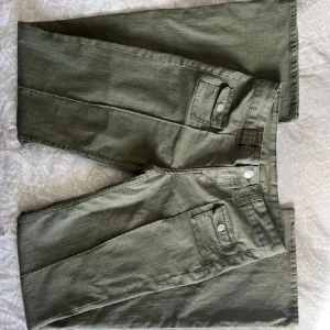 Gröna bootcut byxor med fickdetaljer - Snygga gröna bootcut byxor med dekorativa fickor och knappar. Byxorna har en lågmidjad passform och är perfekta nu till våren. Säljer då de inte används längre. De har en liten defekt(sista bilden) men inget som märks!💕