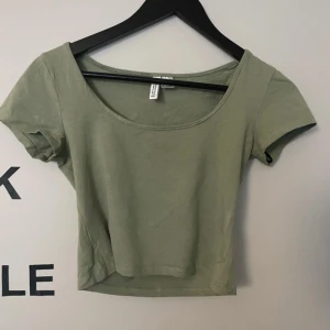 Olivgrön kortärmad topp från H&M - Snygg olivgrön topp från H&m med korta ärmar och rund halsringning. Perfekt för en avslappnad stil. Passar bra till jeans eller kjol.