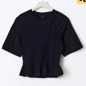 Svart kortärmad topp med rynkdetaljer - Snygg svart topp med korta ärmar och rynkdetaljer över bröstet. Perfekt för en stilren look. Den har en lätt volang vid nederkanten som ger en extra touch. Helt ny från Gina tricot med prislapp kvar. Är mer som en S än M