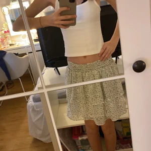 Grön och vit blommig kjol - Söt kortkjol i grönt och vitt med blommigt mönster. Perfekt för varma dagar med sin luftiga och bekväma passform. Resår i midjan för extra komfort.