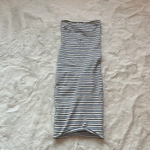 Randig klänning från Gina Tricot - Säljer en snygg randig klänning från Gina Tricot i storlek S. Klänningen är axelbandslös och har ett stilrent mönster i svart, vitt och blått. Perfekt för en somrig look!