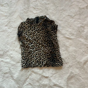 Leopardmönstrad topp från Moves x NA-KD - Säljer en snygg leopardmönstrad topp från Moves x NA-KD. Toppen har korta ärmar och en dragkedja i ryggen för en smidig passform. Perfekt för att ge din outfit en trendig touch 🐆