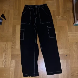 Svarta cargopants med kontrastsömmar - Snygga svarta cargopants med vita kontrastsömmar. Byxorna har flera praktiska fickor och en hög midja. 