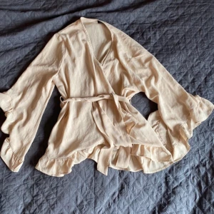 Puderrosa omlottblus  - Puderrosa omlottblus med volanger. Luftig och skön att ha på sommaren eller på stranden.  Obs! Förekommer en svart fläck på skärpet, syns dock inte när du har på dig plagget 