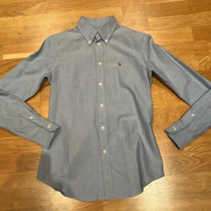 Tvärfet skjorta från Polo Ralph Lauren - Snygg blå skjorta från Polo Ralph Lauren med klassisk krage och broderad logotyp på bröstet💯 Skjortan har långa ärmar och knappar framtill. Perfekt för en stilren look nu till sommaren☀️✅. Om du har frågor elelr funderingar så svarar jag gärna😊