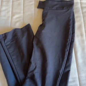 Svarta byxor från Nelly - Snygga svarta byxor från Nelly med låg midja och stilren design. Byxorna har en rak passform och stängs med knappar framtill. Perfekta för en chic look. Sköna som yoga pant men snygga som kostymbyxor 