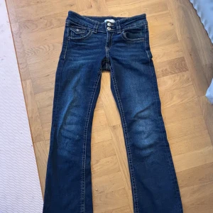Lågmidjade  bootcut jeans - Snygga blå bootcut jeans med låg midja och klassisk femficksdesign. Jeansen har en dragkedja och knappar framtill. Perfekta för en avslappnad stil.