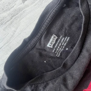 Svart t-shirt från Levi's - Säljer en svart t-shirt från Levi's med deras ikoniska röda logga på bröstet. Perfekt för en casual look. T-shirten är kortärmad och gjord i mjuk bomull. Passar till det mesta och är ett måste i garderoben! BEHÖVER STRYKAS och rollas, hund finns i hemmet!