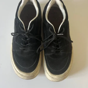 Svarta sneakers med lila detaljer - Snygga svarta sneakers i mocka från Eytts med vita sulor och lila detaljer på hälen. Skorna har snörning och en unik hjärtformad detalj på sulan. Perfekta för en stilren look.