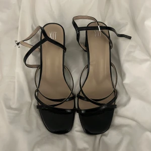 Svarta sandaler med klack från XIT - Eleganta svarta sandaler med klack och smala remmar från XIT. Skorna har en fyrkantig tå och justerbara remmar för en perfekt passform. Perfekta för en stilren look. Jag själv har 38/39 i skor men dessa va små i storleken då jag behövde gå upp i strl. Använd endast 1 gång 