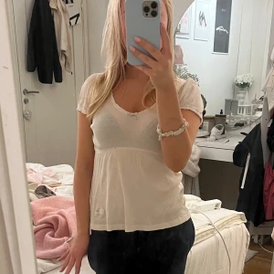 Beige topp från Odd Molly - Säljer en söt beige topp från Odd Molly med korta ärmar och ribbad struktur. Toppen har fina spetsdetaljer vid halsringningen och ärmsluten samt ett broderat märke på ärmen. Perfekt för en avslappnad stil.