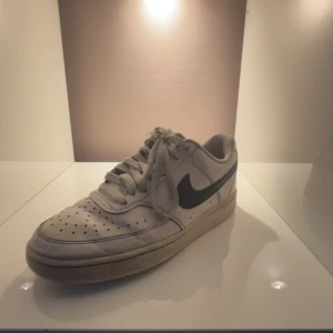 Nike skor - Säljer ett par klassiska vita Nike sneakers med svart swoosh. Skorna har snörning och perforerade detaljer på tån för extra ventilation. 