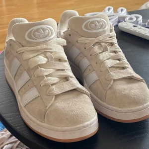 Beige sneakers Adidas Campus 00s - Snygga beige sneakers från Adidas med klassiska vita ränder och en gummisula. Använda endast ett fåtal gånger då vi köpt fel stl. Skon har snörning och är perfekta för en avslappnad stil. Fungerande qrkod. 