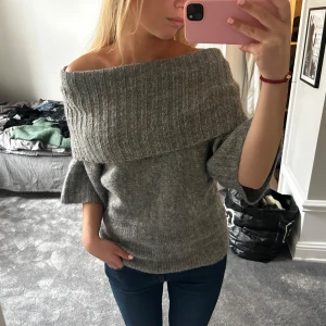 Grå stickad offshoulder tröja - Säljer en mysig grå stickad tröja med offshoulder-design. Tröjan har trekvartsärmar och en bred krage som kan bäras både uppe och nere. Perfekt för en stilren och avslappnad look.