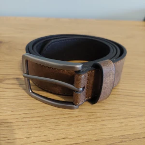 Brunt skärp med silverfärgat spänne - Snyggt brunt skärp i skinn med ett stilrent silverfärgat spänne. Perfekt för att komplettera din outfit med en klassisk touch. Skärpet har flera hål för justerbar passform.