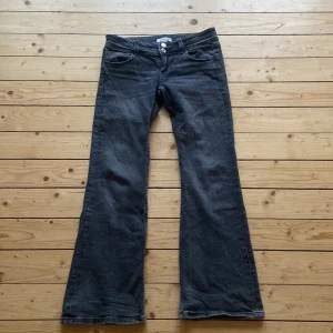 Grå/svarta bootcut jeans från Gina Tricot - Snygga svarta bootcut jeans från Gina Tricot. De har en klassisk femficksdesign med knappar fram och bakfickor med lock. Perfekta för en stilren look. Använt 3 gånger. Säljer pågrund av fel storlek 💕
