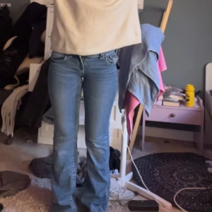 Lågmidjade jeans från Gina Tricot - Säljer ett par snygga blå jeans från Gina Tricot. De har en bootcut-stil och är tillverkade i ett klassiskt denimtyg. Perfekta för en avslappnad look med en touch av retro. Jeansen har fickor både fram och bak samt knappar i midjan. Jätte fina storlek 158 och Lågmidjade. Enda skavanken är nere vid slutet av jeansen som man kan se på sista bilden.