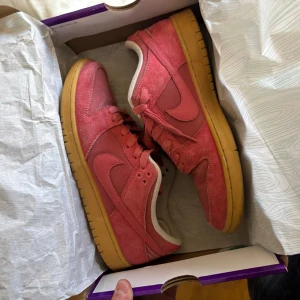  Nike dunk low Adobe - Säljer ett par snygga röda sneakers från Nike med en klassisk design. Skorna har en gul sula och är tillverkade i mocka med snörning. Perfekta för en avslappnad stil. Finns med kvitto direkt från junkyard Stockholm